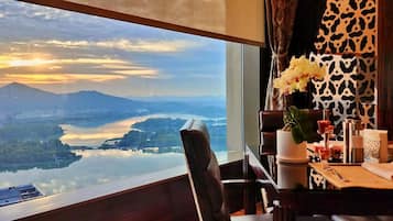 A hotel room with a large window offering a scenic view of a lake, mountains, and a cityscape.