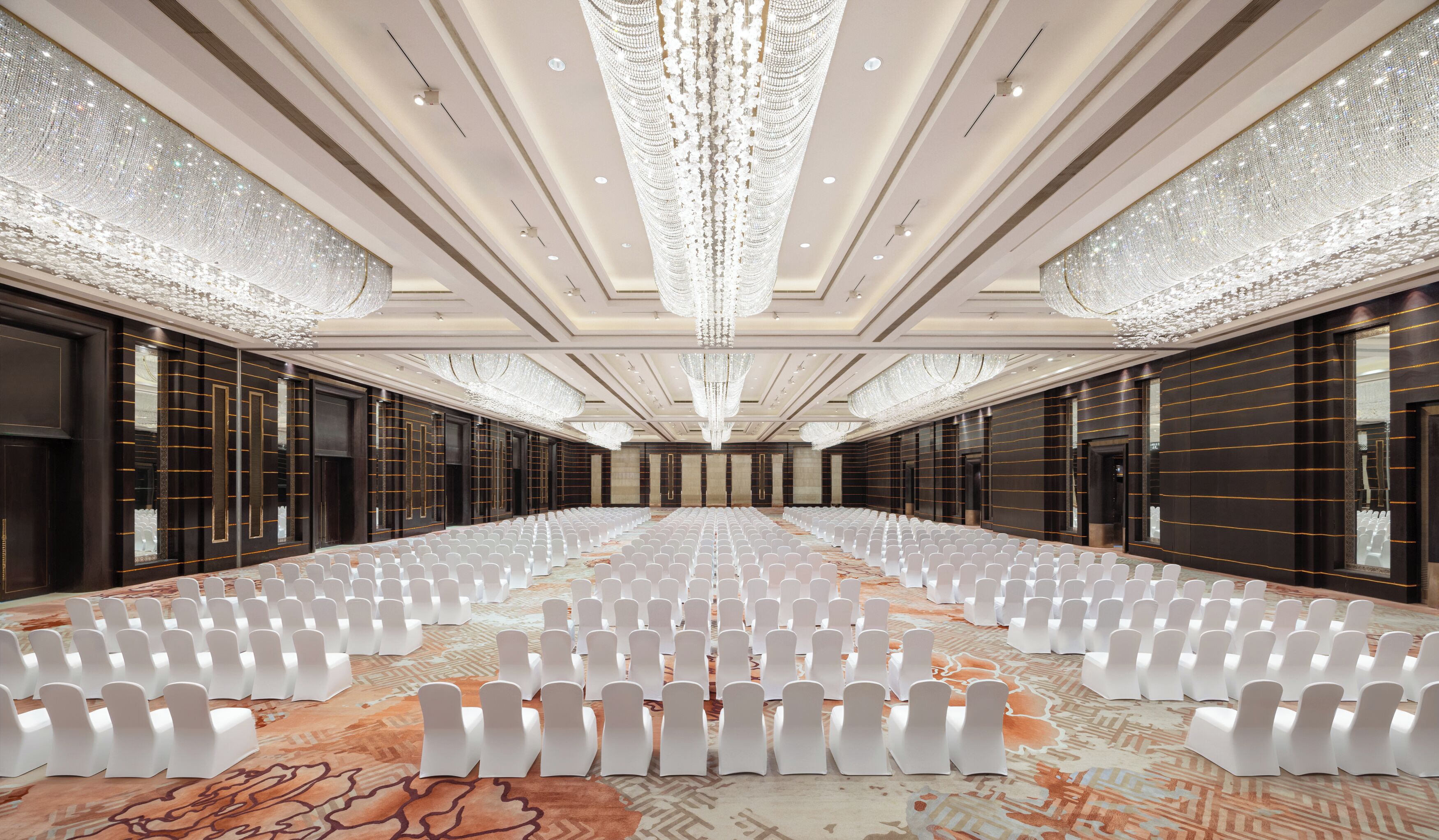 Une vaste salle de conférence avec des rangées de chaises blanches, une moquette à motifs et de somptueux lustres.