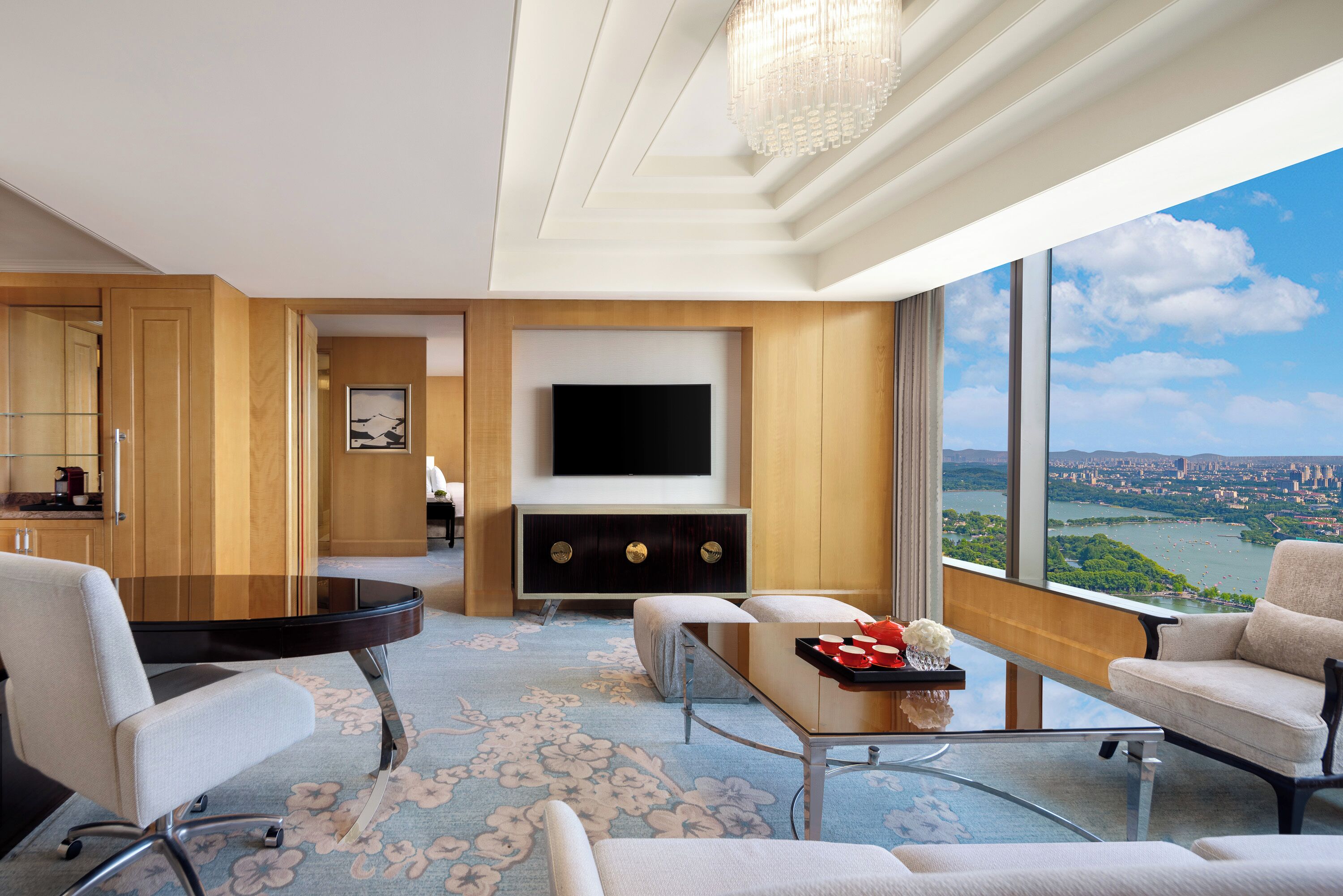 A modern hotel room with a large TV, comfortable seating, a dining area, and a scenic view of a city and river.