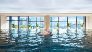 Una amplia piscina interior con vistas a la ciudad, rodeada de plantas en macetas.