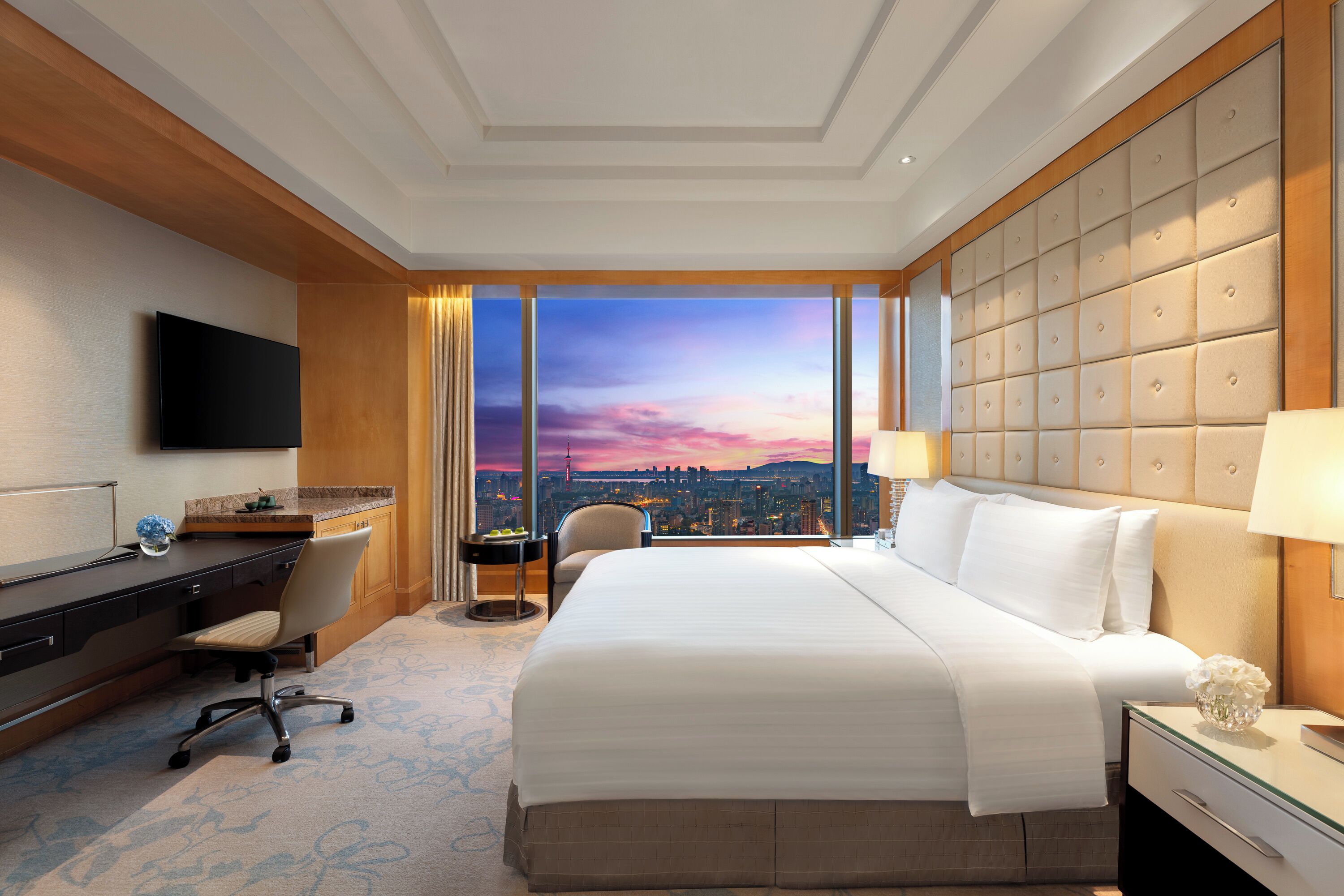 A hotel room with a large bed, a desk, a chair, and a TV.