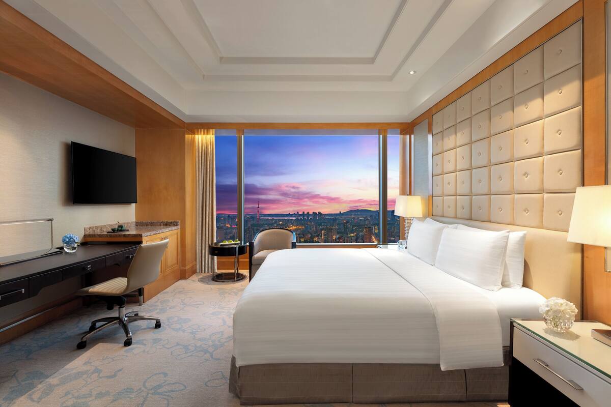 Ein Hotelzimmer mit einem großen Bett, einem Schreibtisch, einem Stuhl und einem Fernseher.