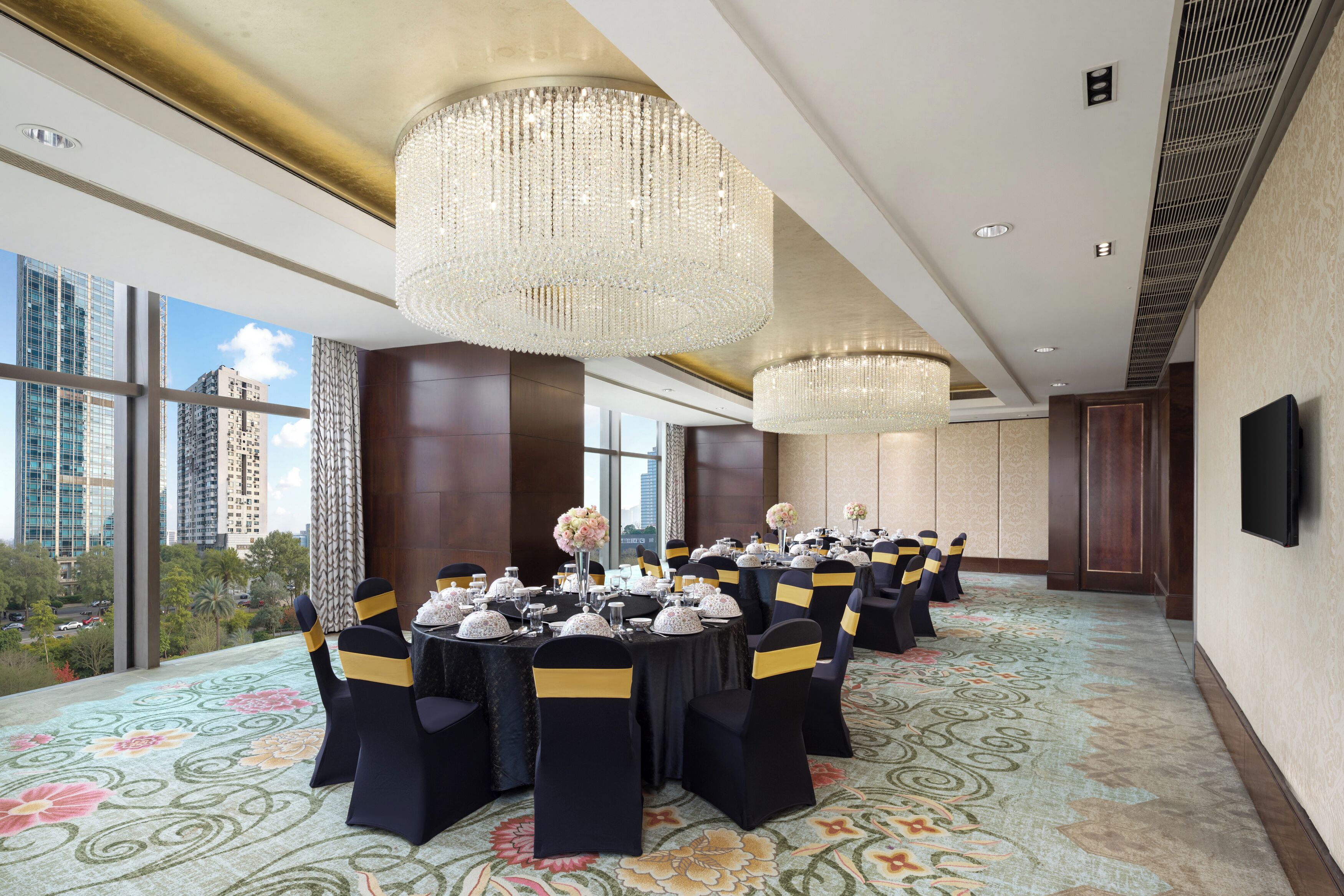 A conference room with round tables, black chairs with yellow sashes, and large chandeliers.