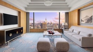 Una sala de estar moderna con un televisor grande, asientos cómodos, una mesita de centro y vistas a la ciudad.