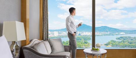 A hotel room with a large window, a sofa, a table with a vase, and a bed.