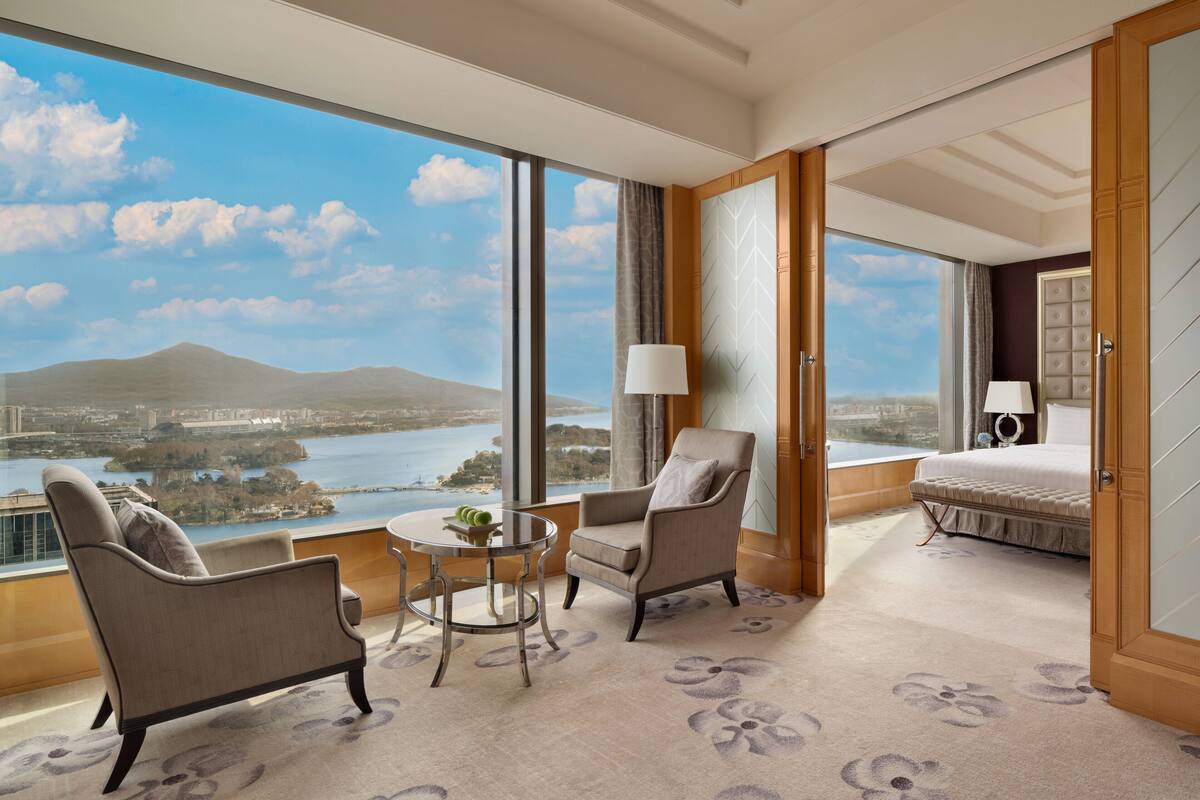 Ein Hotelzimmer mit großem Fenster und Blick auf die Stadt, inklusive Bett, Stuhl, kleinem Tisch und Lampe.
