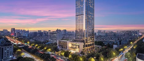 Um edifício alto com fachada de vidro moderna, cercado por paisagem urbana e ruas movimentadas.
