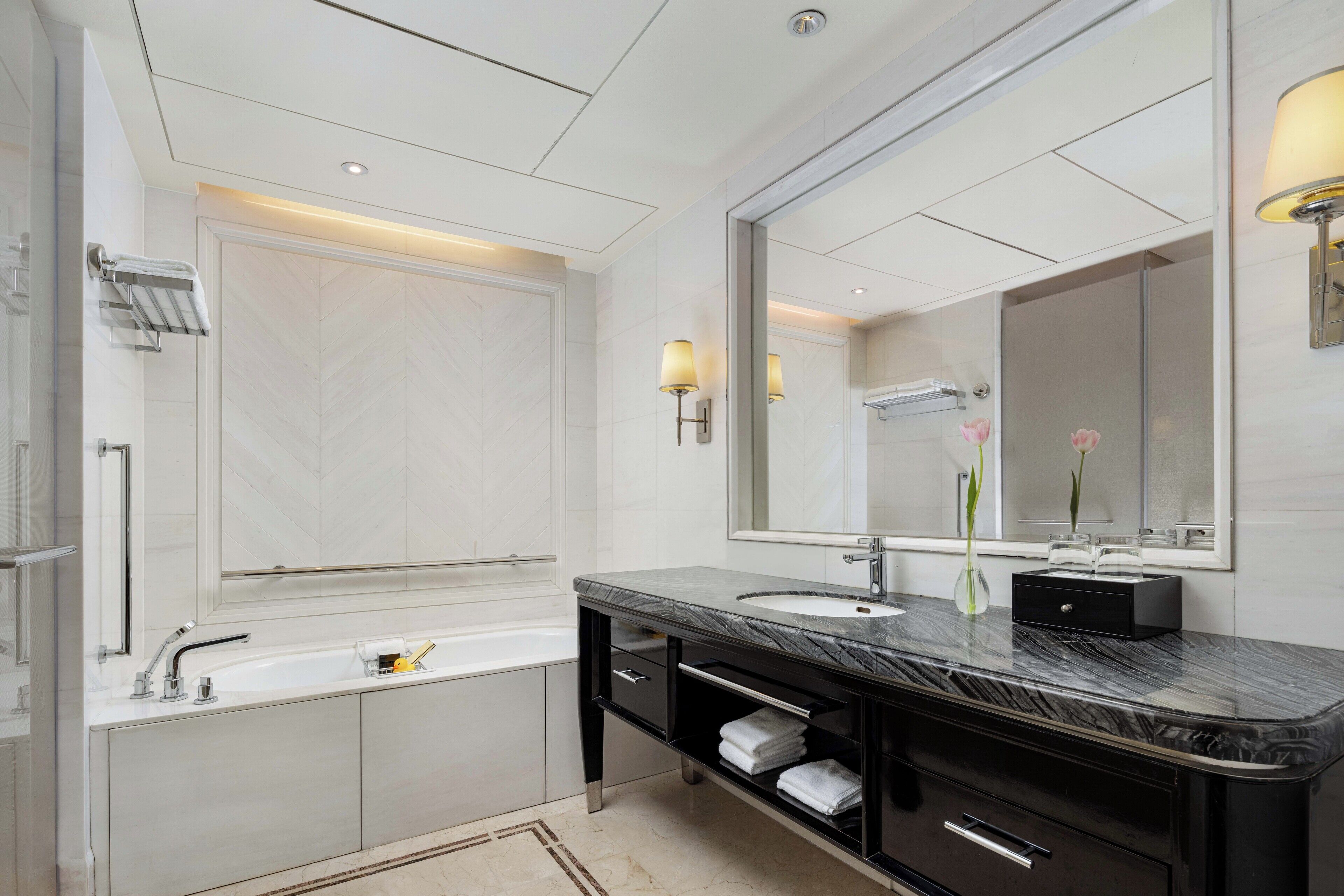 A modern bathroom with a large mirror, a bathtub, and a vanity with a sink.