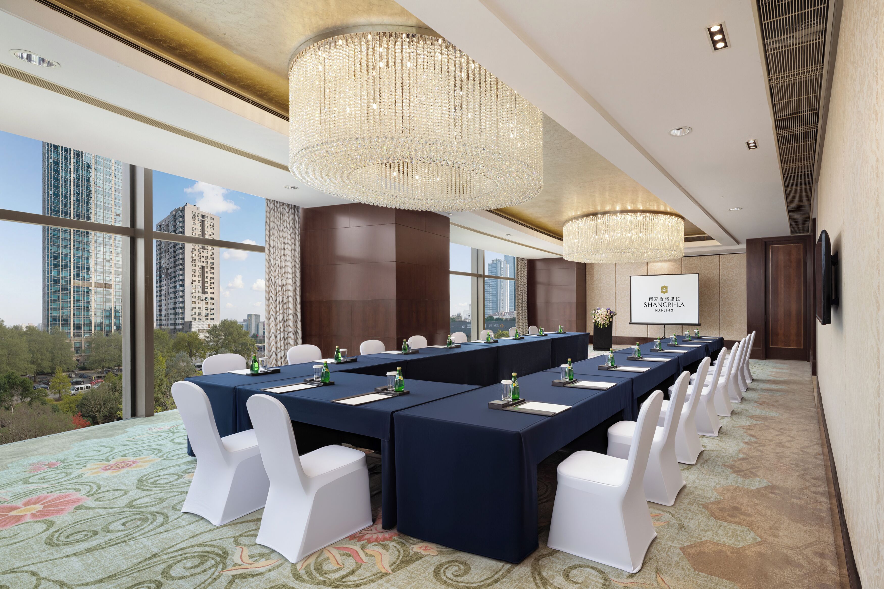 Une salle de conférence avec une longue table, des chaises blanches et un grand lustre.