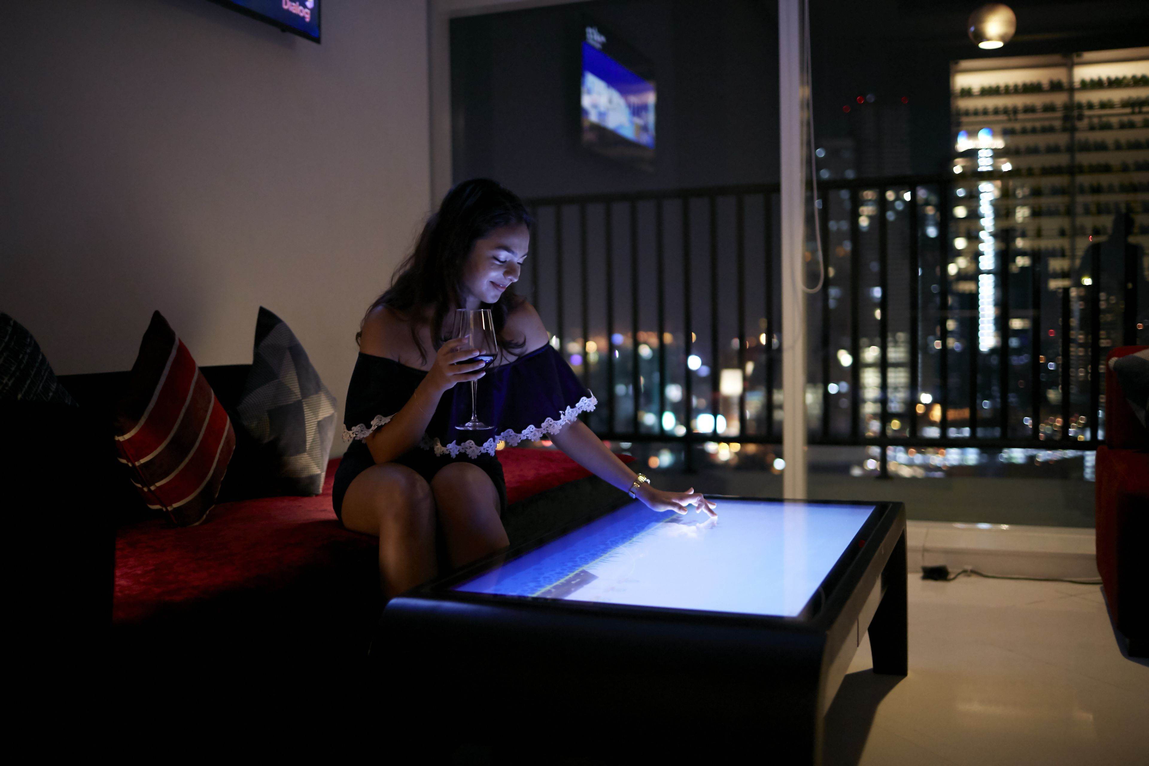 A person sitting on a red couch with a glass of wine, using a tablet on a table.