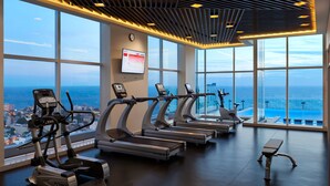 A gym with treadmills, an elliptical, and a stationary bike, overlooking a city and the sea. - Cinnamon Red Colombo (Colombo)