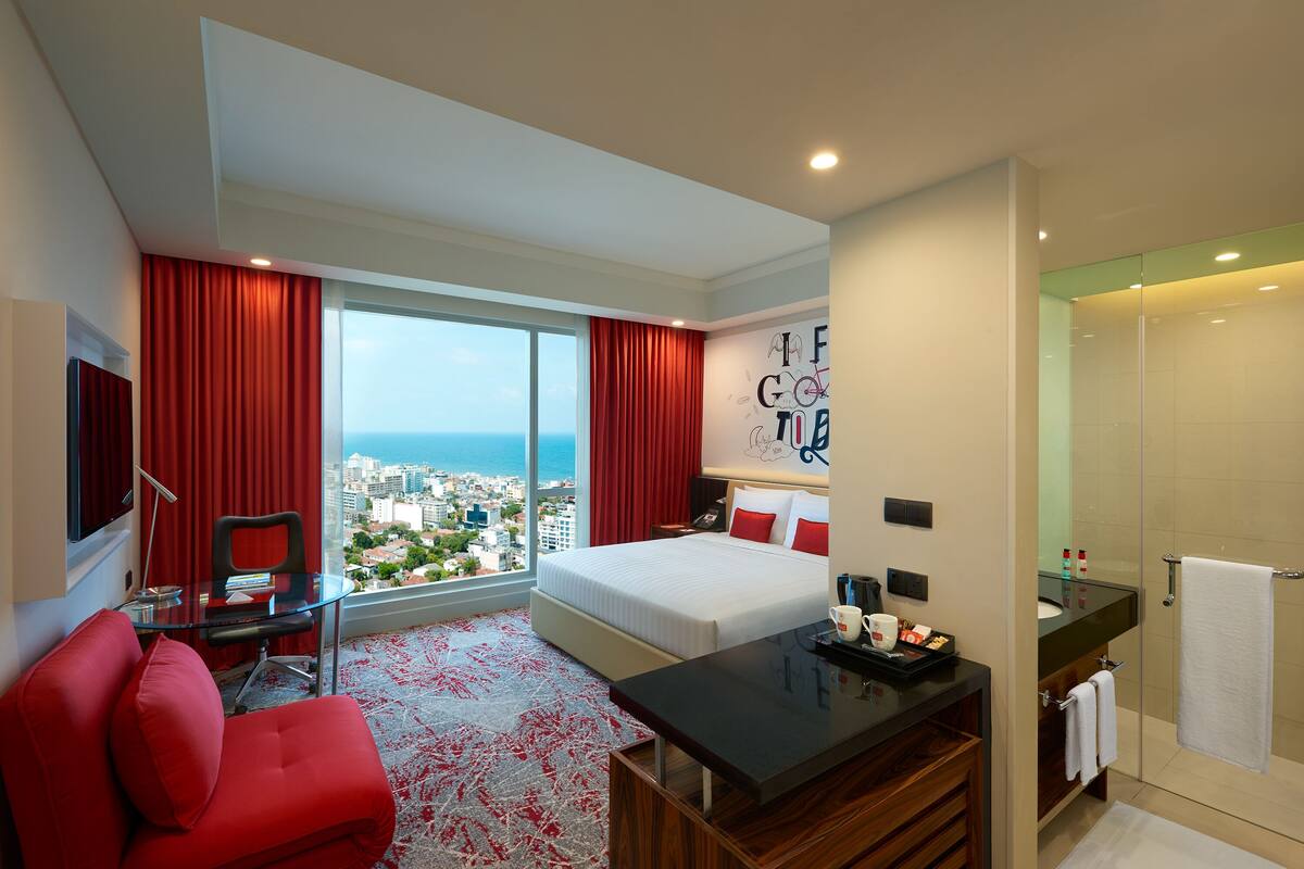 Una habitación de hotel con una cama grande, un escritorio con silla, televisión y vistas a la ciudad.