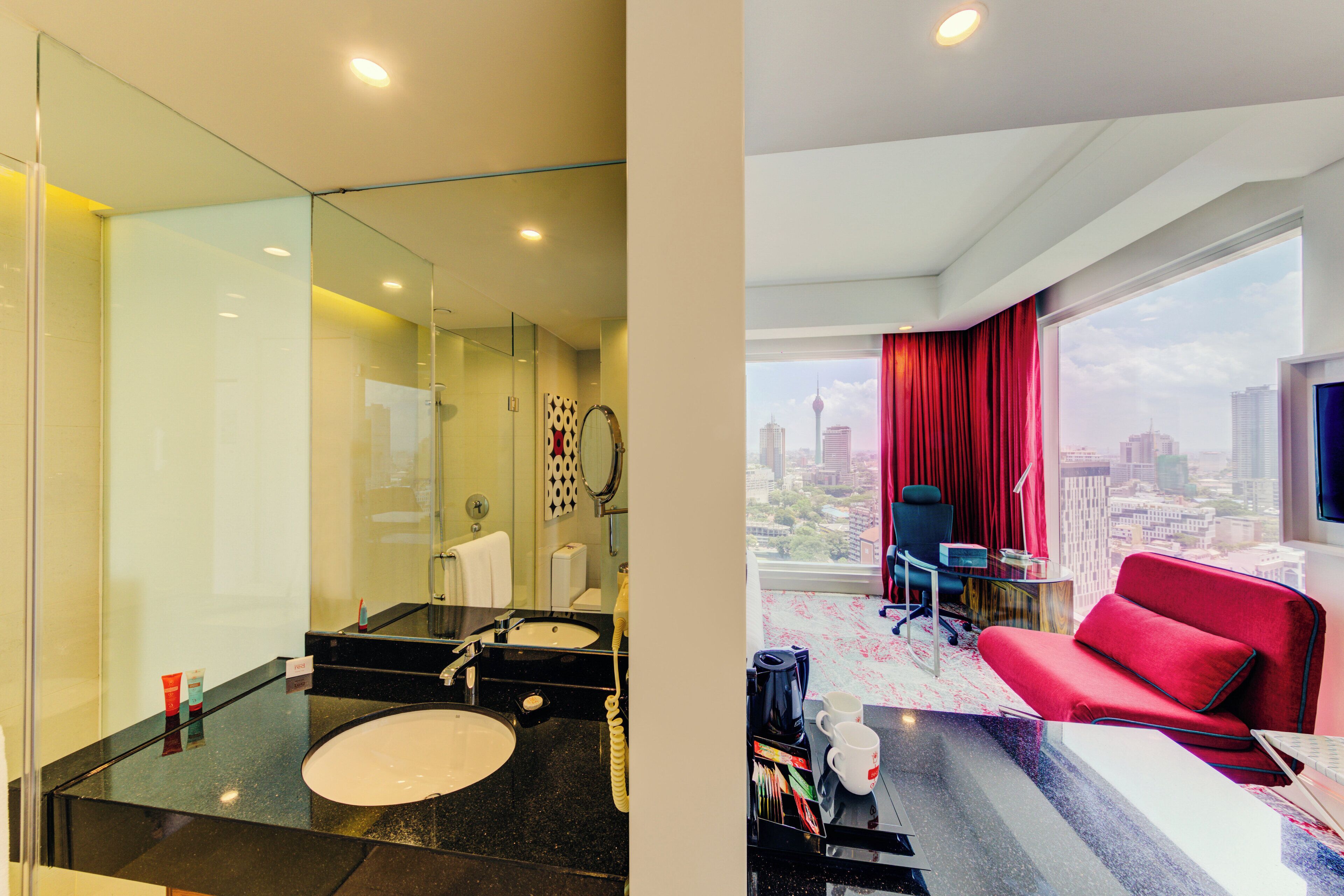 A modern hotel room with a large window, a red sofa, and a city view.