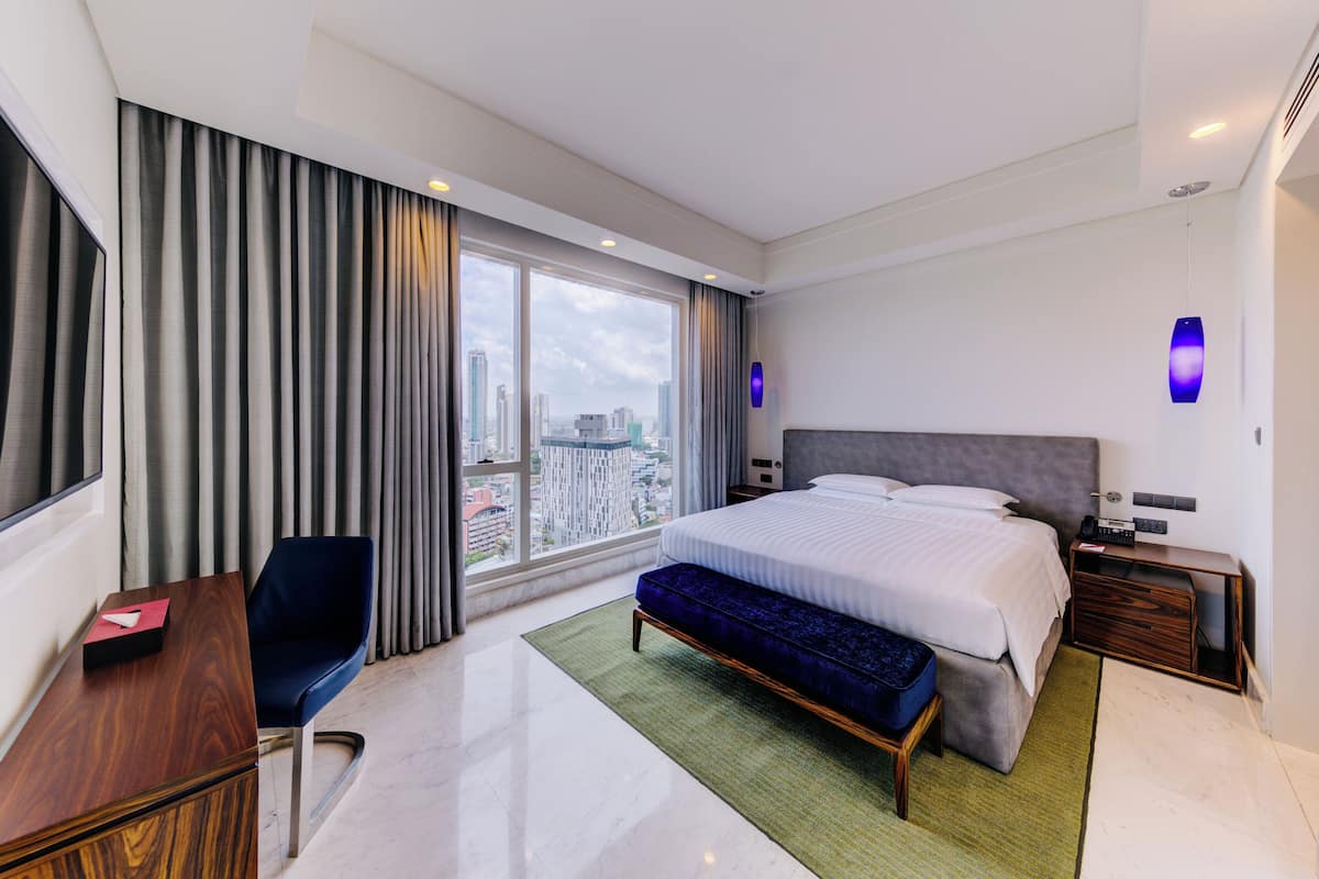 Habitación de hotel moderna con una cama grande, un escritorio, una silla y vistas a la ciudad a través del ventanal.