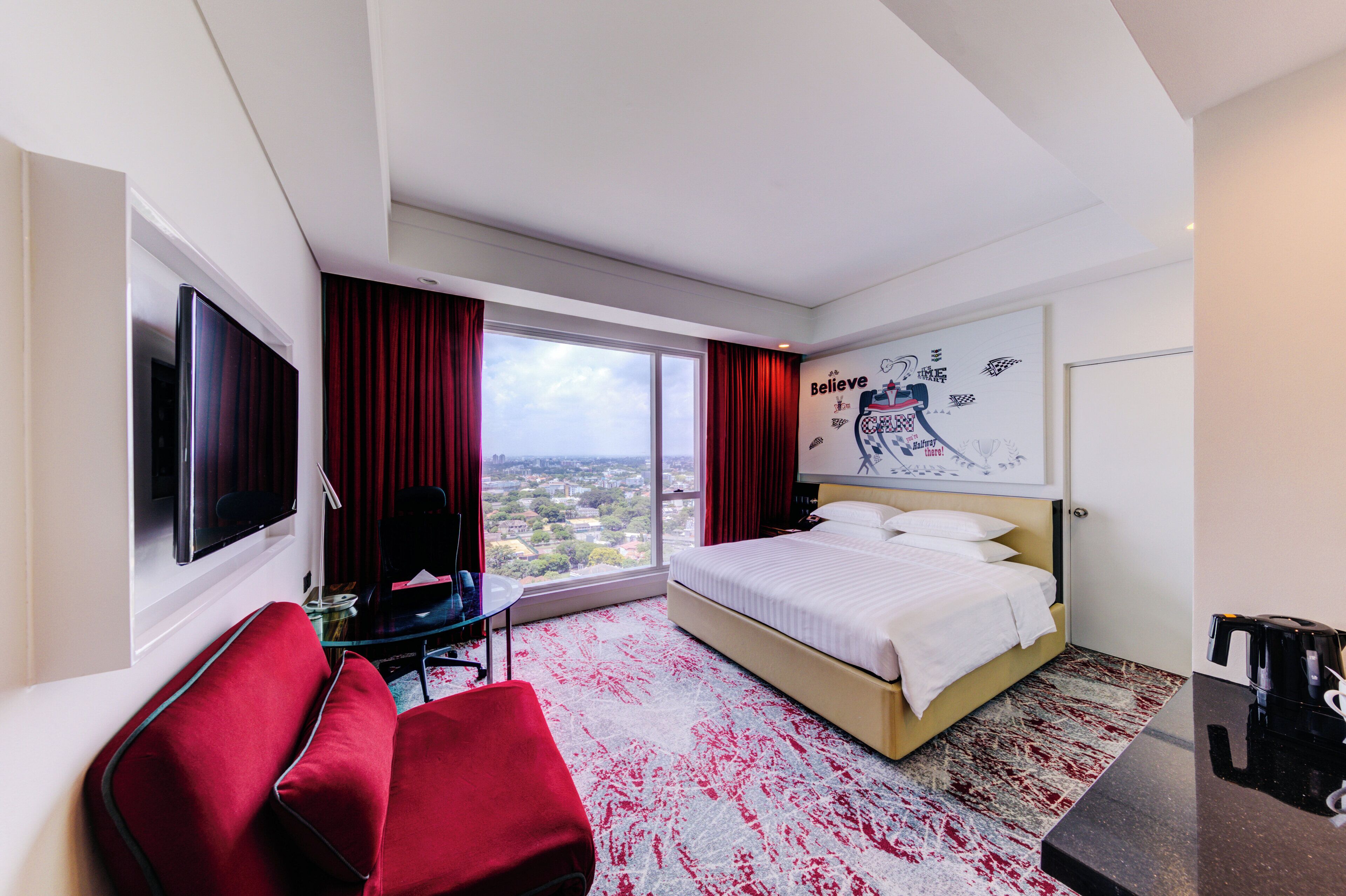 A hotel room with a bed, a TV, a desk, and a view of the city.