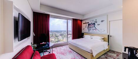 A hotel room with a bed, a TV, a desk, and a view of the city.