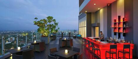 A rooftop bar with a city view, tables, chairs, and a bartender.