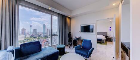 A modern hotel room with a large window offering a city view, a flat-screen TV, a sofa, a coffee table, and a bed with a headboard.