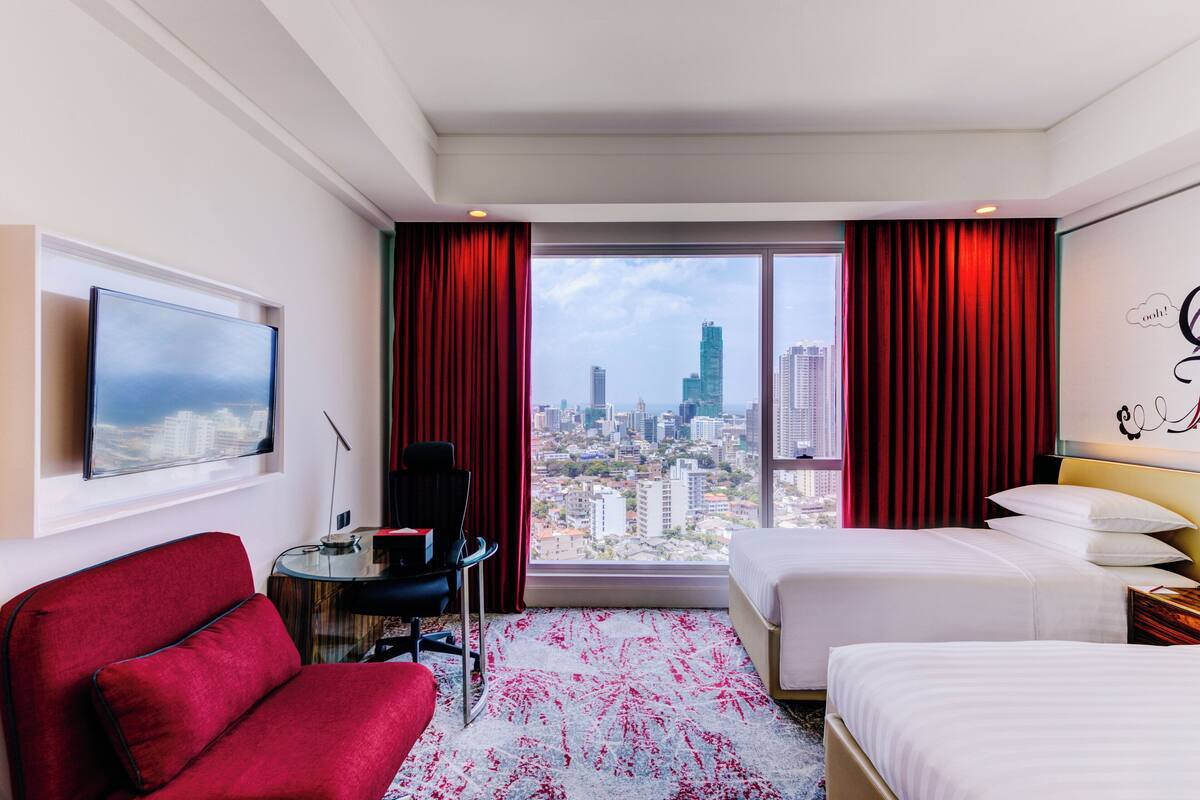 Habitación de hotel con vista a la ciudad, una cama, un escritorio y un sofá rojo.