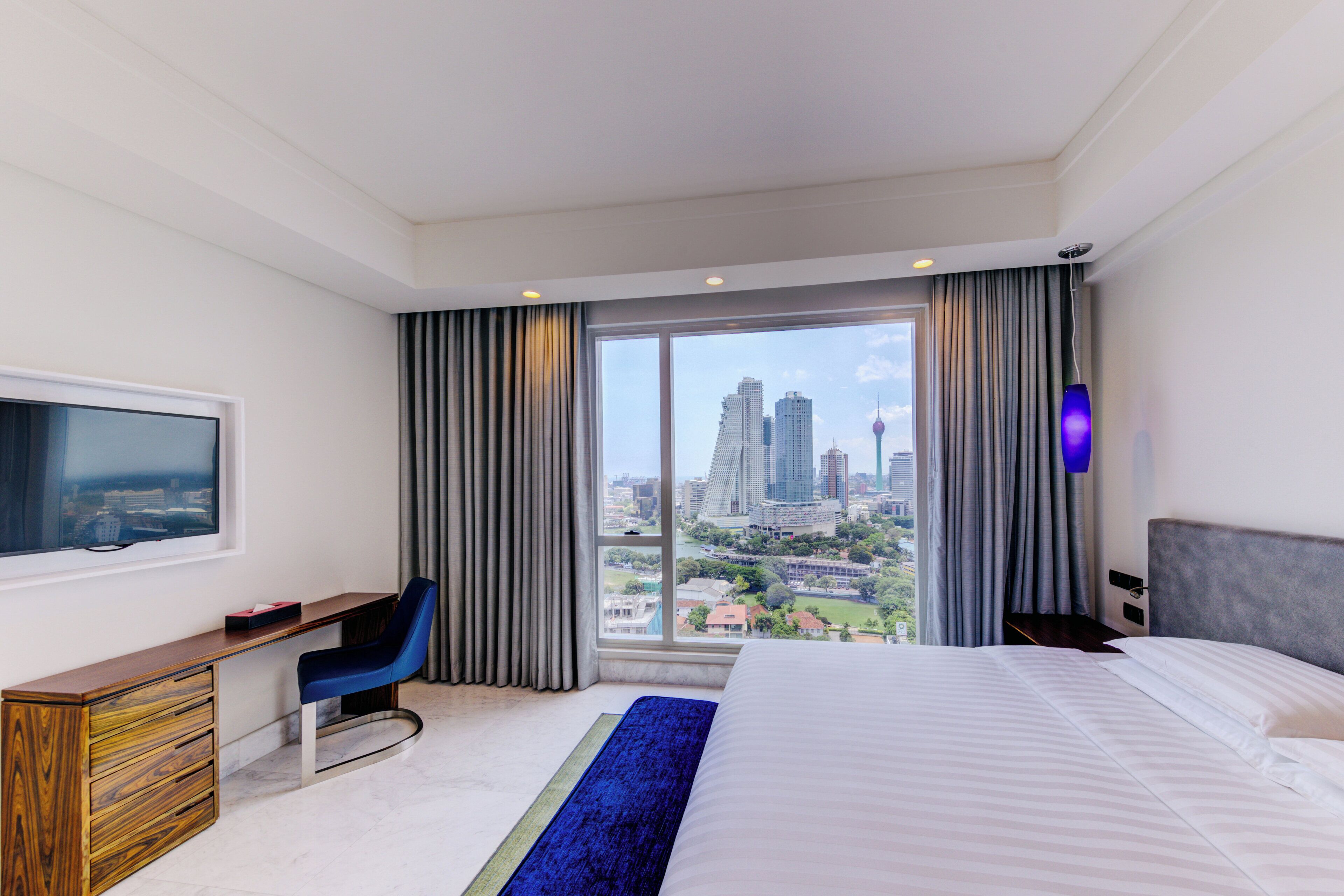 A modern hotel room with a large bed, a desk, and a view of the cityscape.