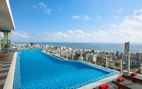 A rooftop infinity pool with a city view, lounge chairs, and a tiled deck.