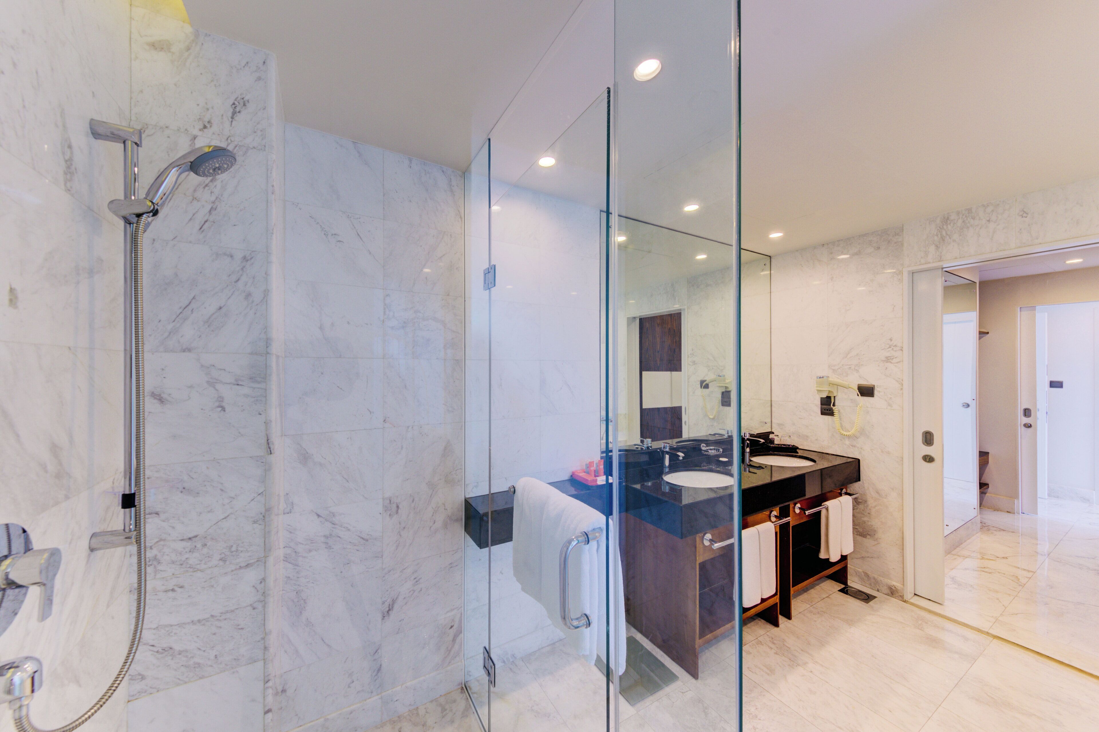 Un baño moderno con ducha envuelta en vidrio, pared con azulejos de mármol, lavamanos con encimera negra y un espejo.