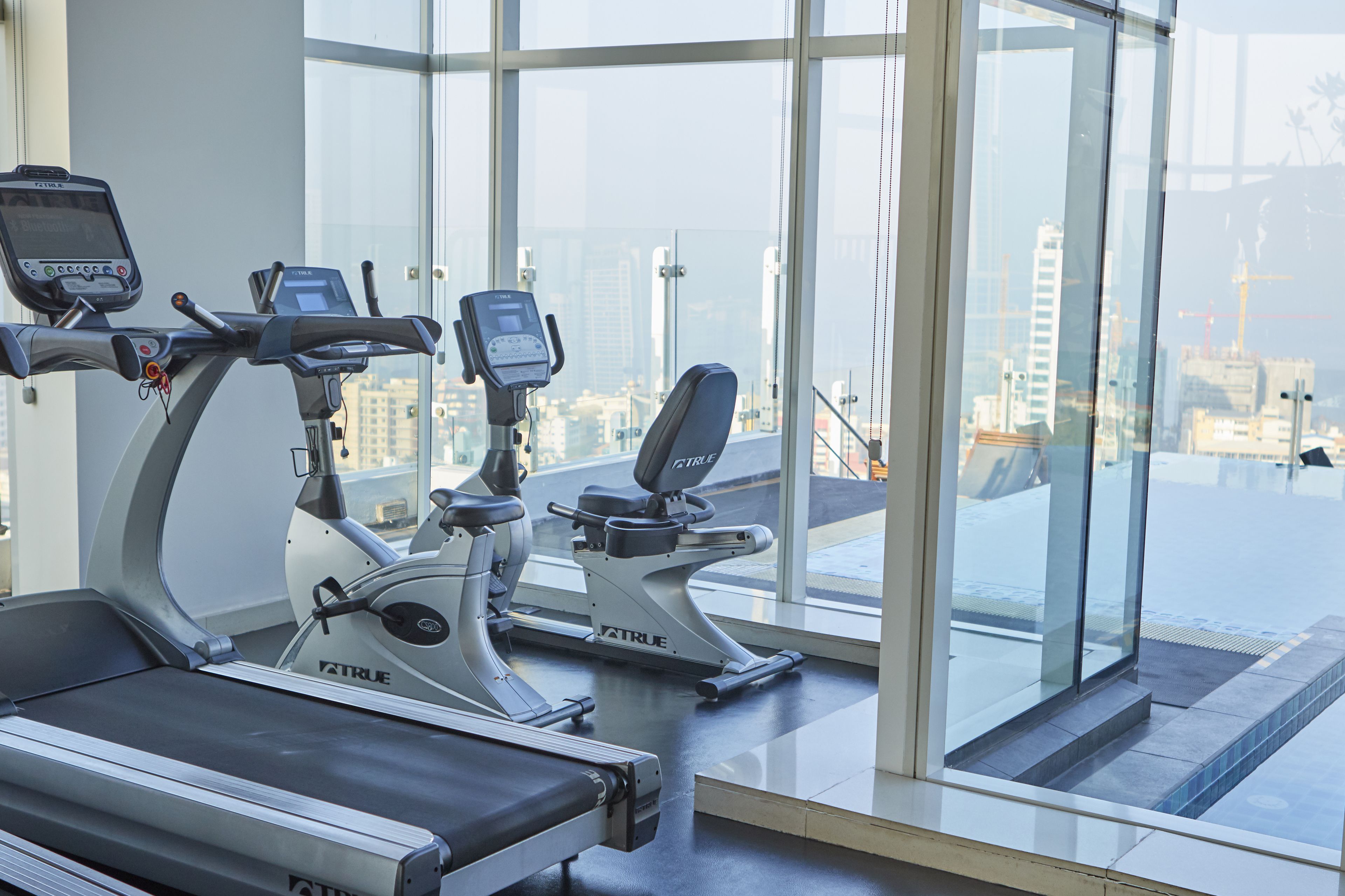 A gym with treadmills and a stationary bike, large windows with a city view.