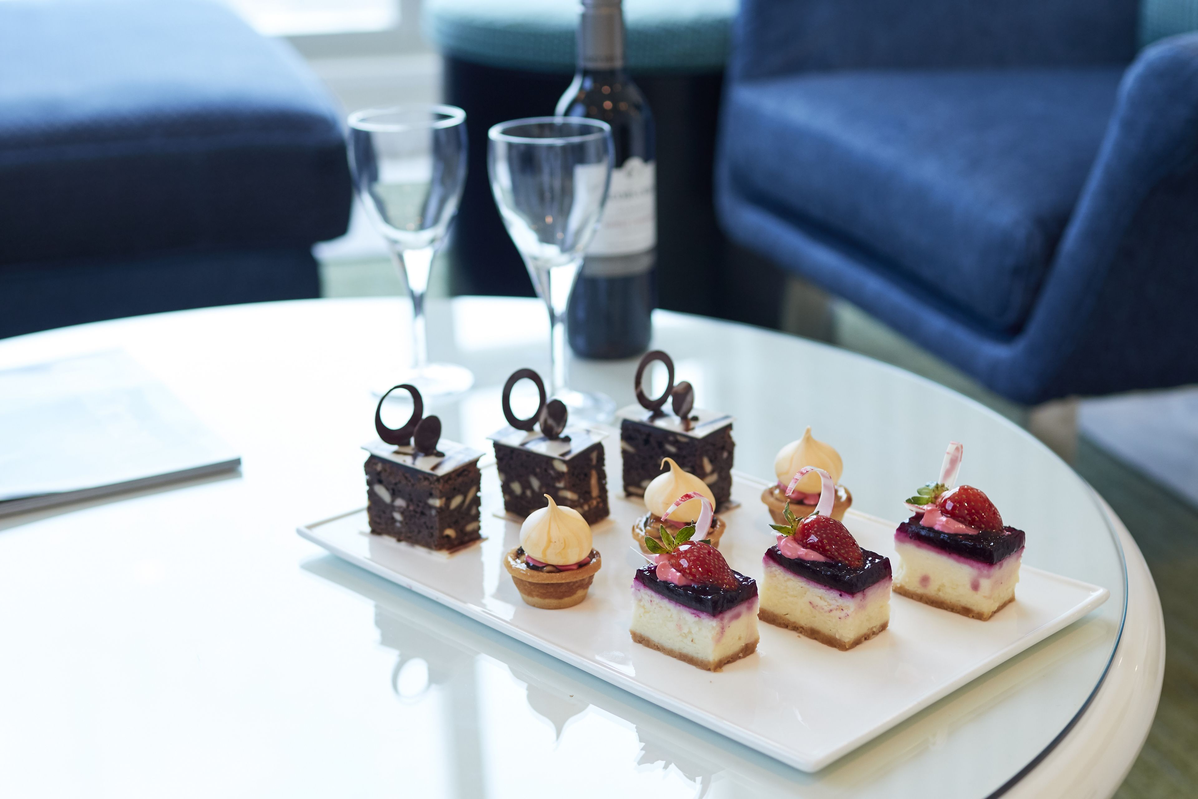 Un plateau de desserts est posé sur une table blanche, avec une bouteille et des verres en arrière-plan.