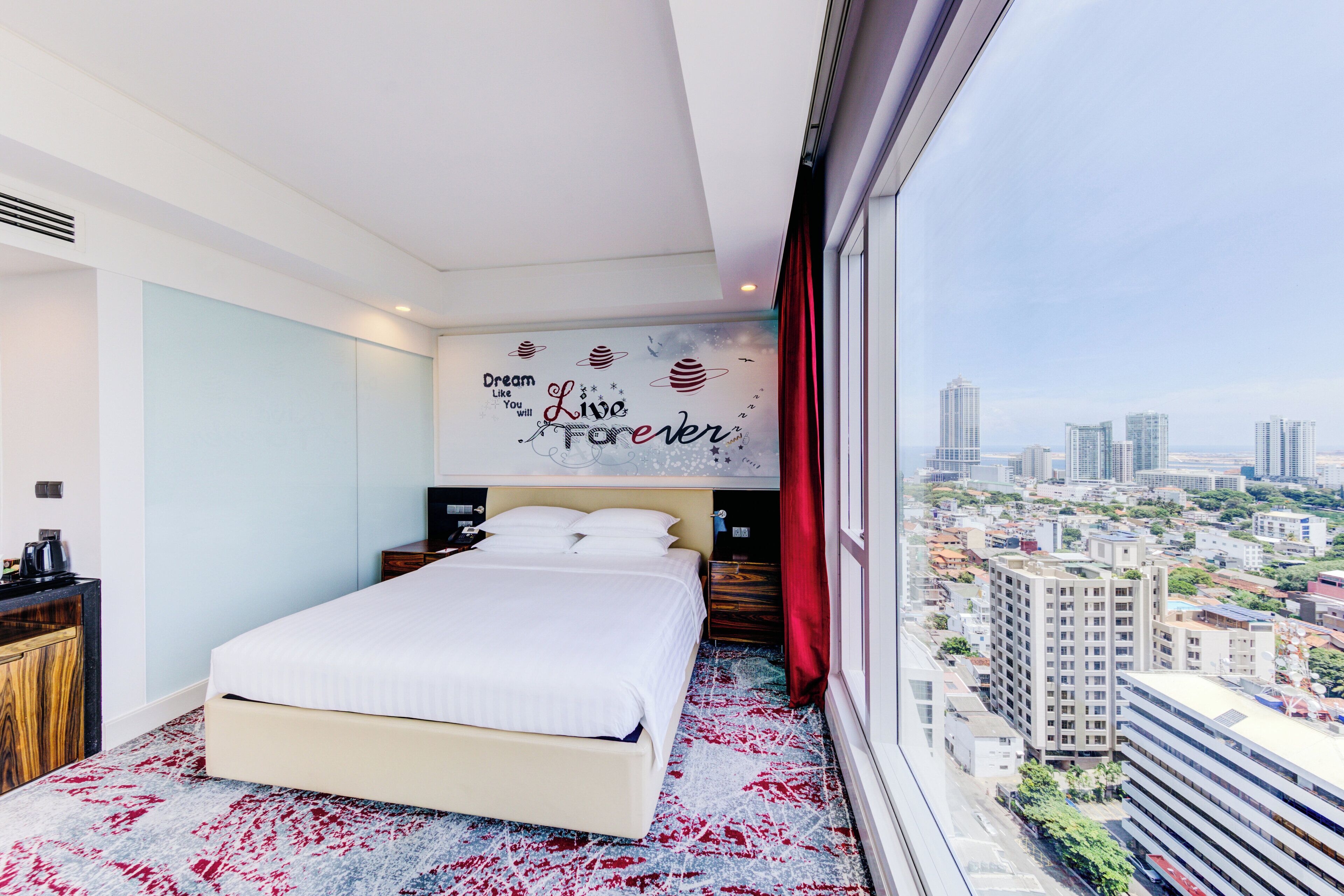 A modern hotel room with a large bed, a city view, and motivational wall art.