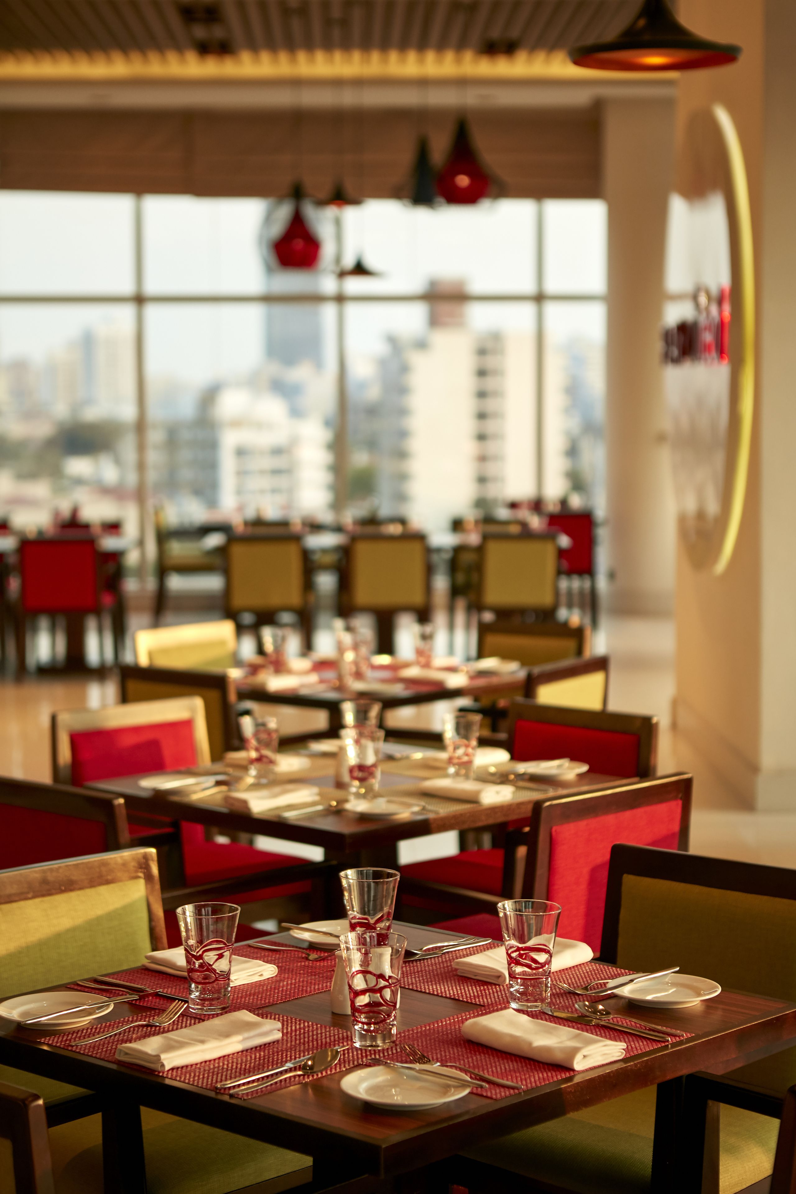 Un espace repas avec des tables dressées, des chaises et une vue sur le paysage urbain grâce à de grandes fenêtres.