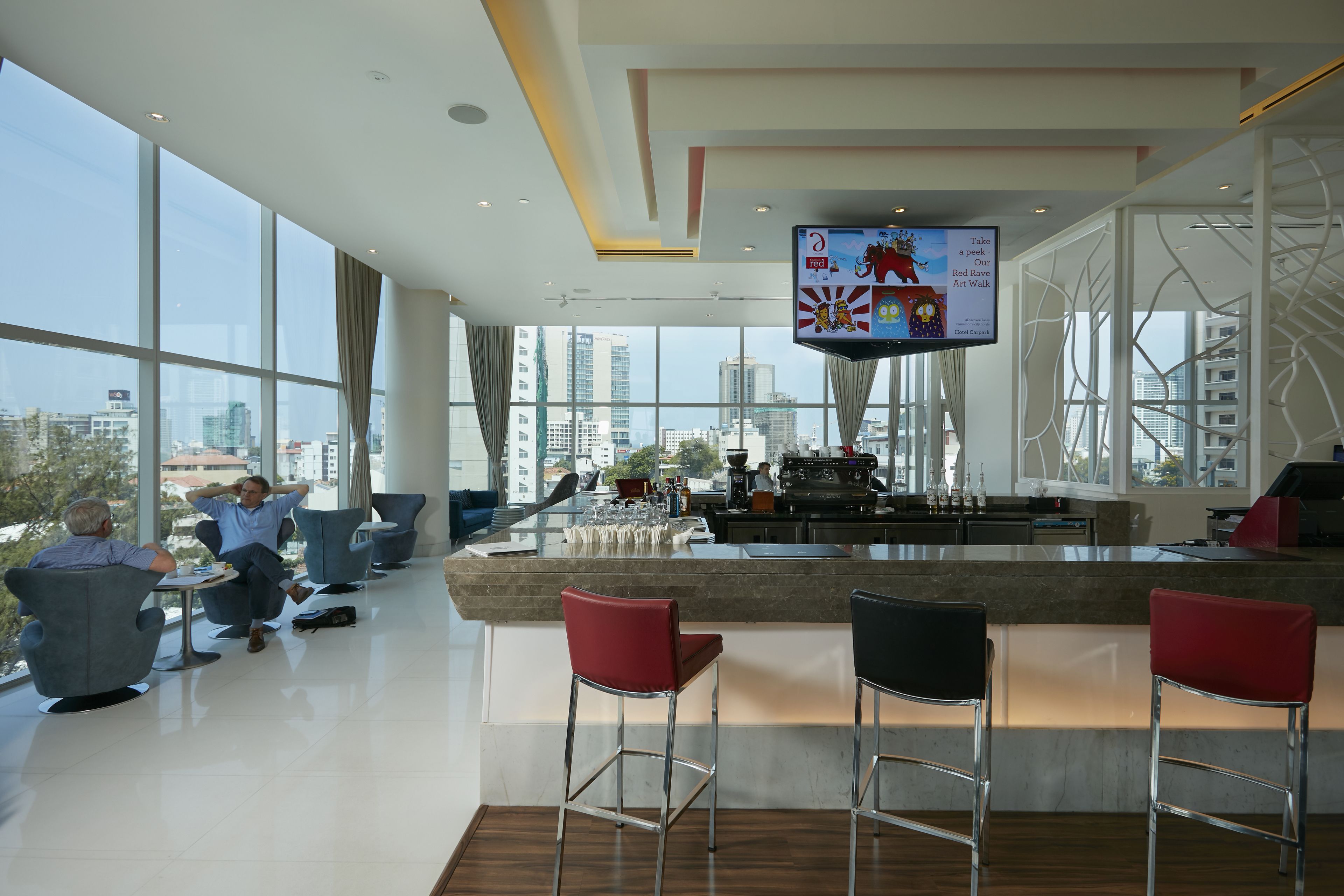 Zona de bar moderna con una pantalla grande, asientos y vistas a la ciudad.