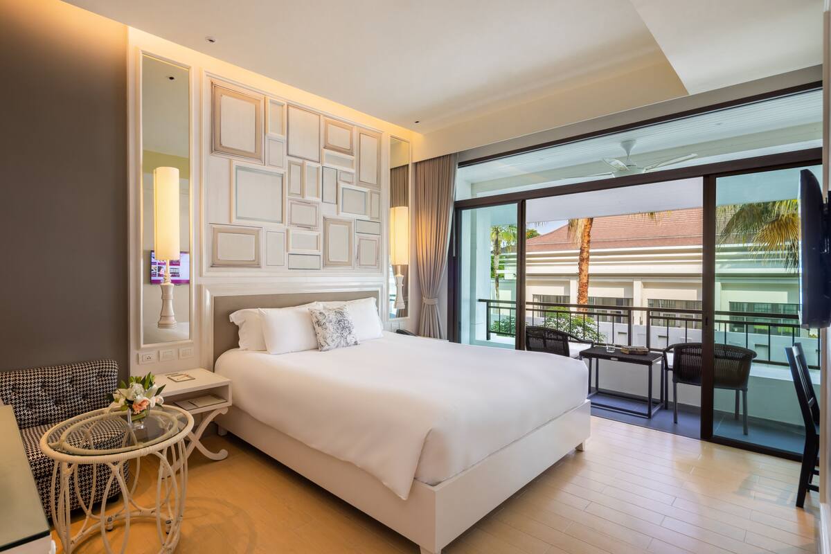Une chambre d’hôtel moderne dotée d’un grand lit, d’une petite table ronde, d’un canapé et d’un balcon avec coin salon extérieur.