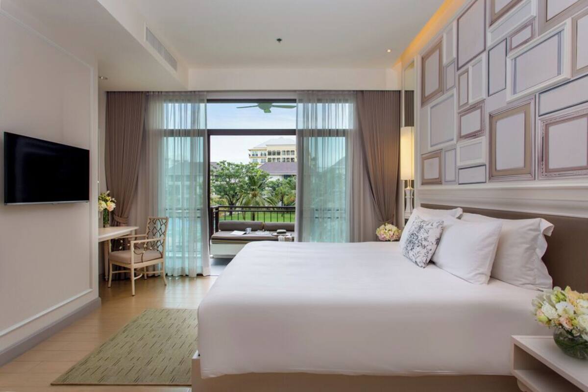 Une chambre d’hôtel avec un grand lit, une télévision, un bureau avec une chaise et un balcon avec des rideaux.