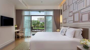 A hotel room with a large bed, a TV, a desk with a chair, and a balcony with curtains.