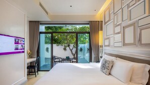 Hotelkamer met een groot bed, een bureau met stoel, een laptop en uitzicht op het groen door een glazen deur.