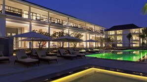 Een hotel met een zwembad, terras en een goed verlichte gevel.