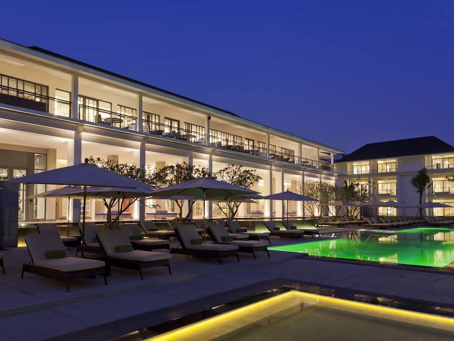 A hotel with a swimming pool, outdoor seating, and a well-lit facade.