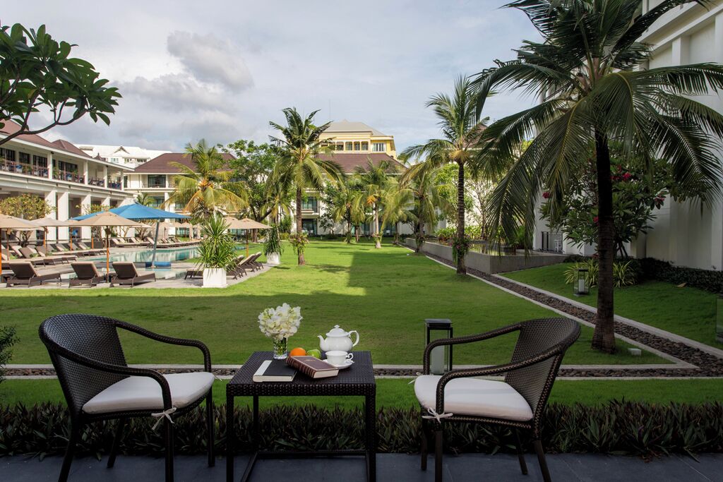 A hotel courtyard with a pool, lounge chairs, and a table with a book and flowers.