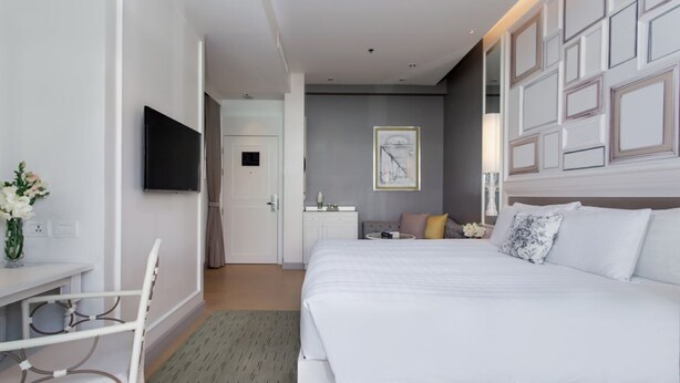 Habitación de hotel con una cama grande, un escritorio con silla, televisor y una mesita con un jarrón de flores.