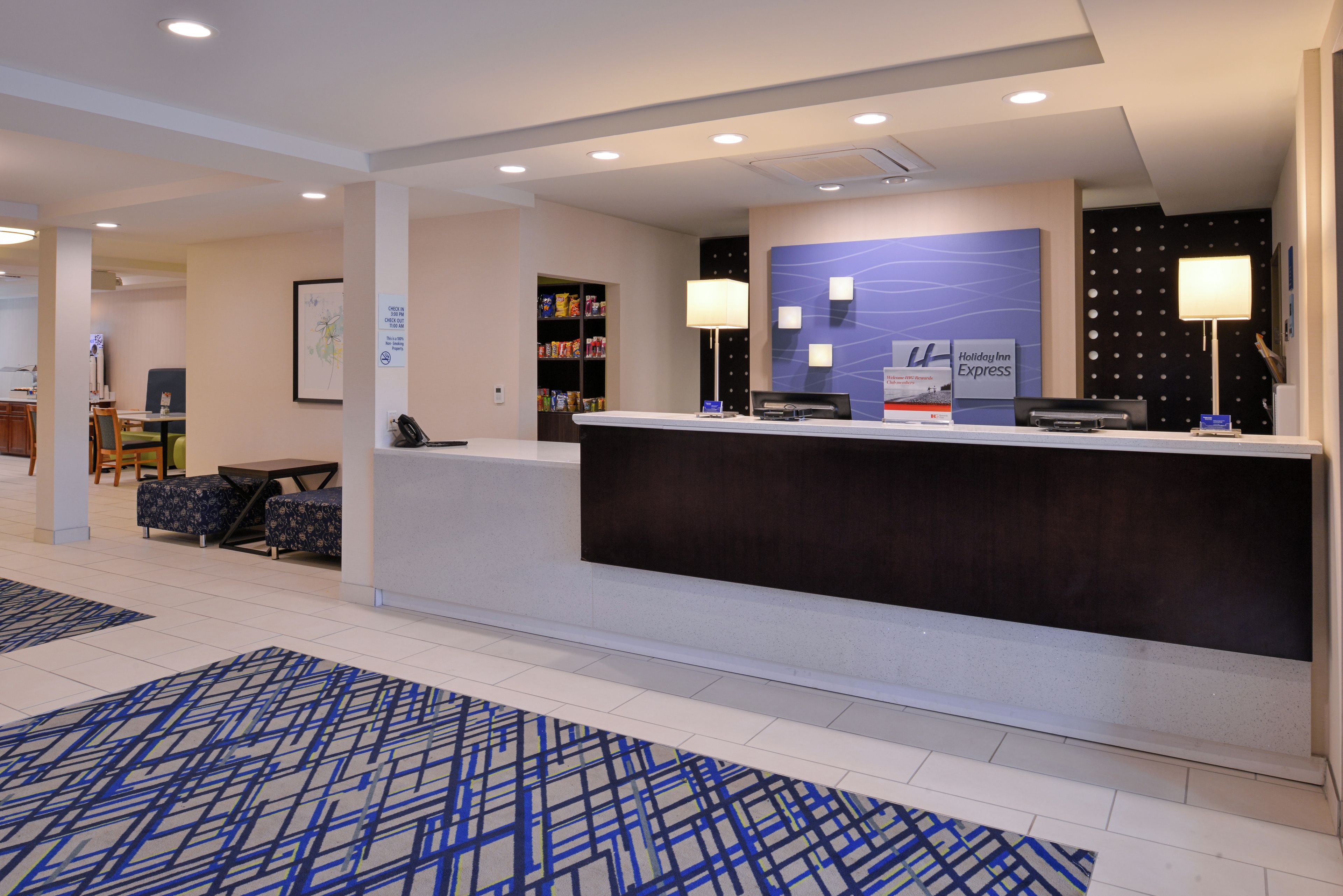 Et hotellets reception med en indtjekningsdisk, et loungeområde med sofa og stole samt en opslagstavle på væggen.