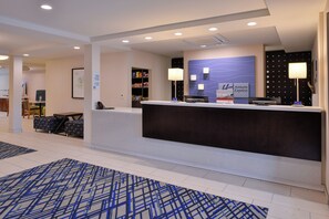 A hotel reception area with a check-in counter, a seating area with a sofa and chairs, and a wall-mounted information board. - Holiday Inn Express & Suites West Ocean City by IHG (Ocean City)