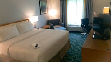 A hotel room with a large bed, a desk with a television, a chair, a lamp, and a window with curtains.