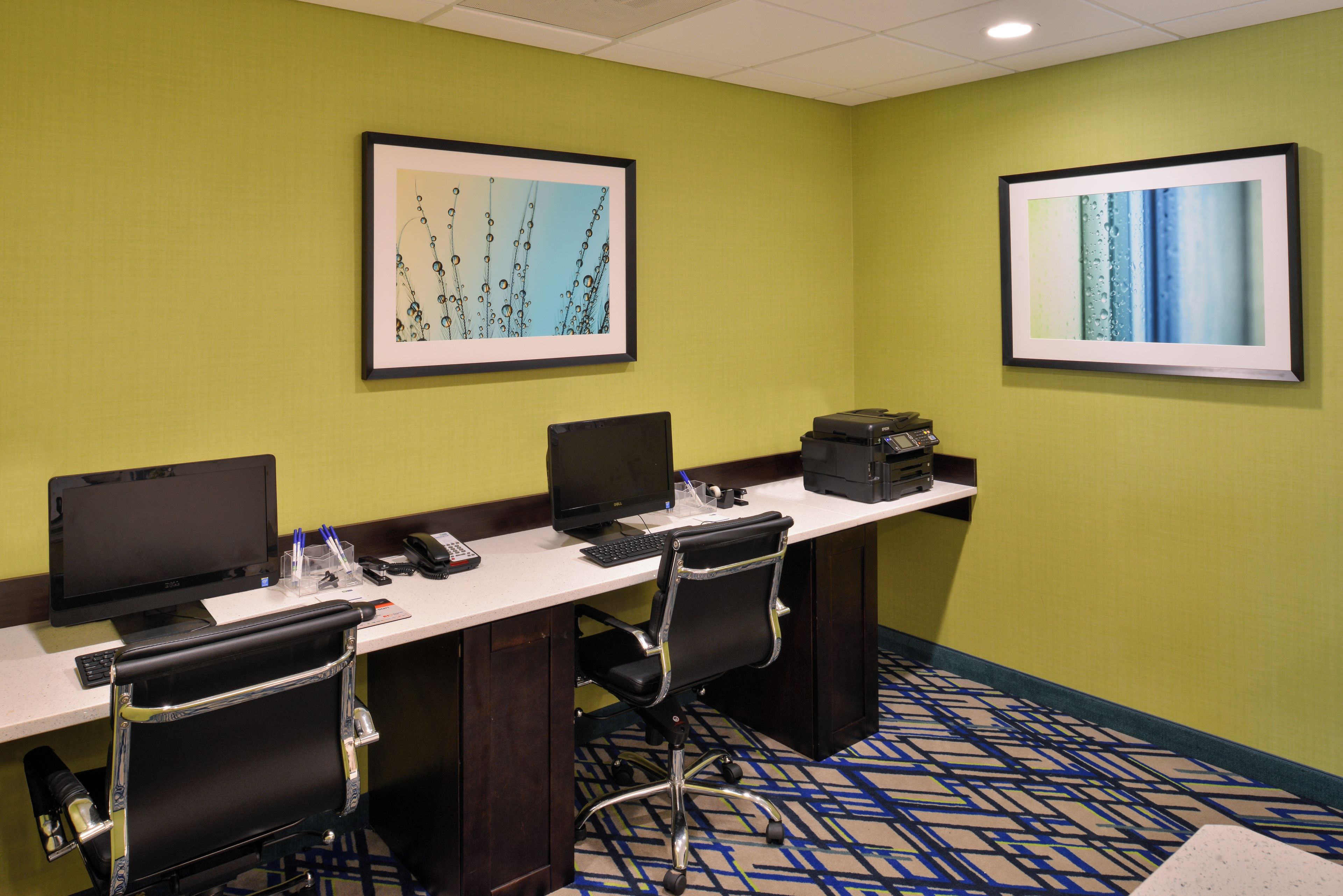 A conference room with a long table, three chairs, two monitors, a telephone, and a printer.