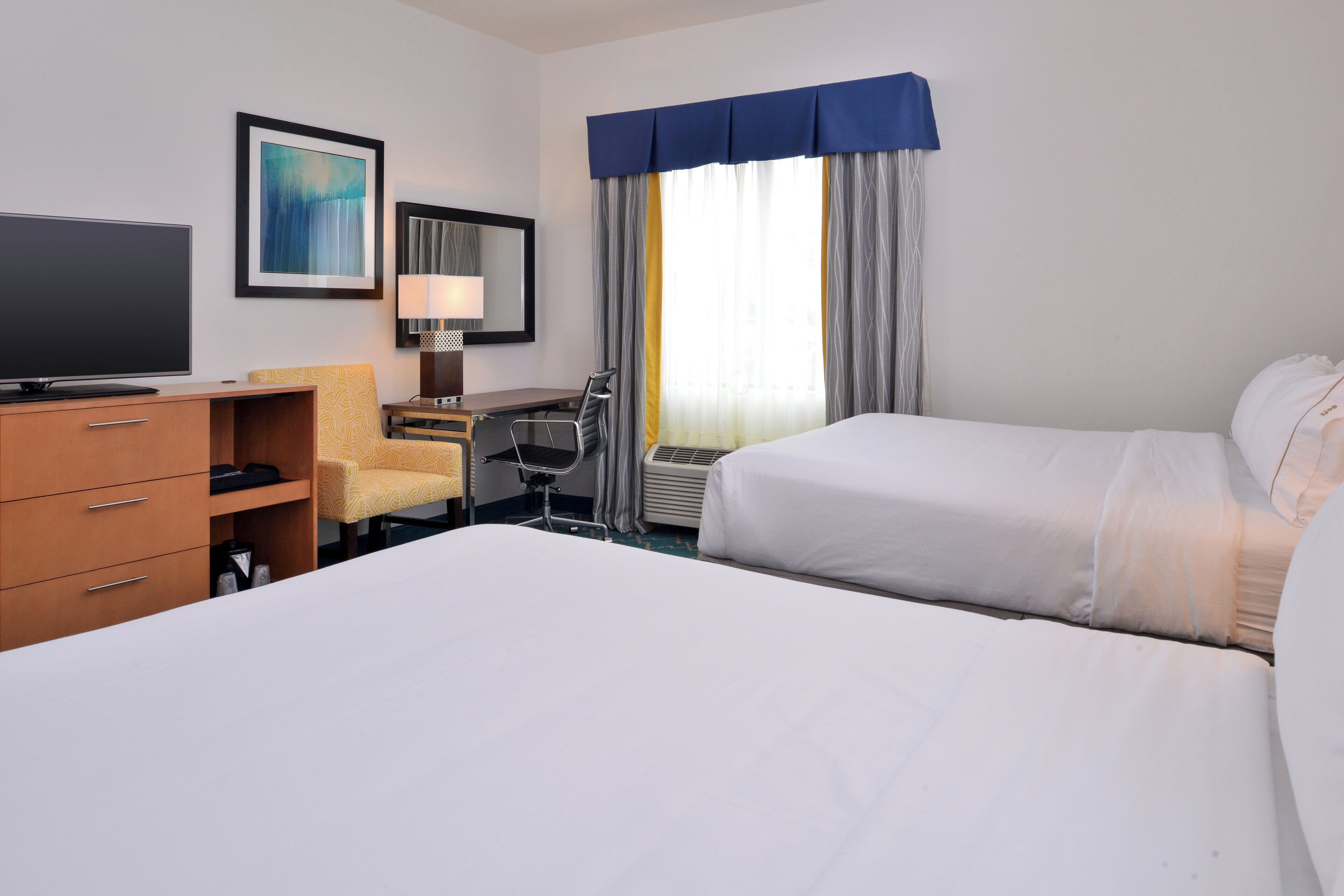 A hotel room with a bed, a desk, a chair, a television, and a window with curtains.
