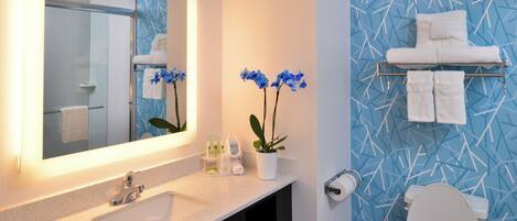 A bathroom with a sink, mirror, towel rack, toilet, and blue patterned wall.