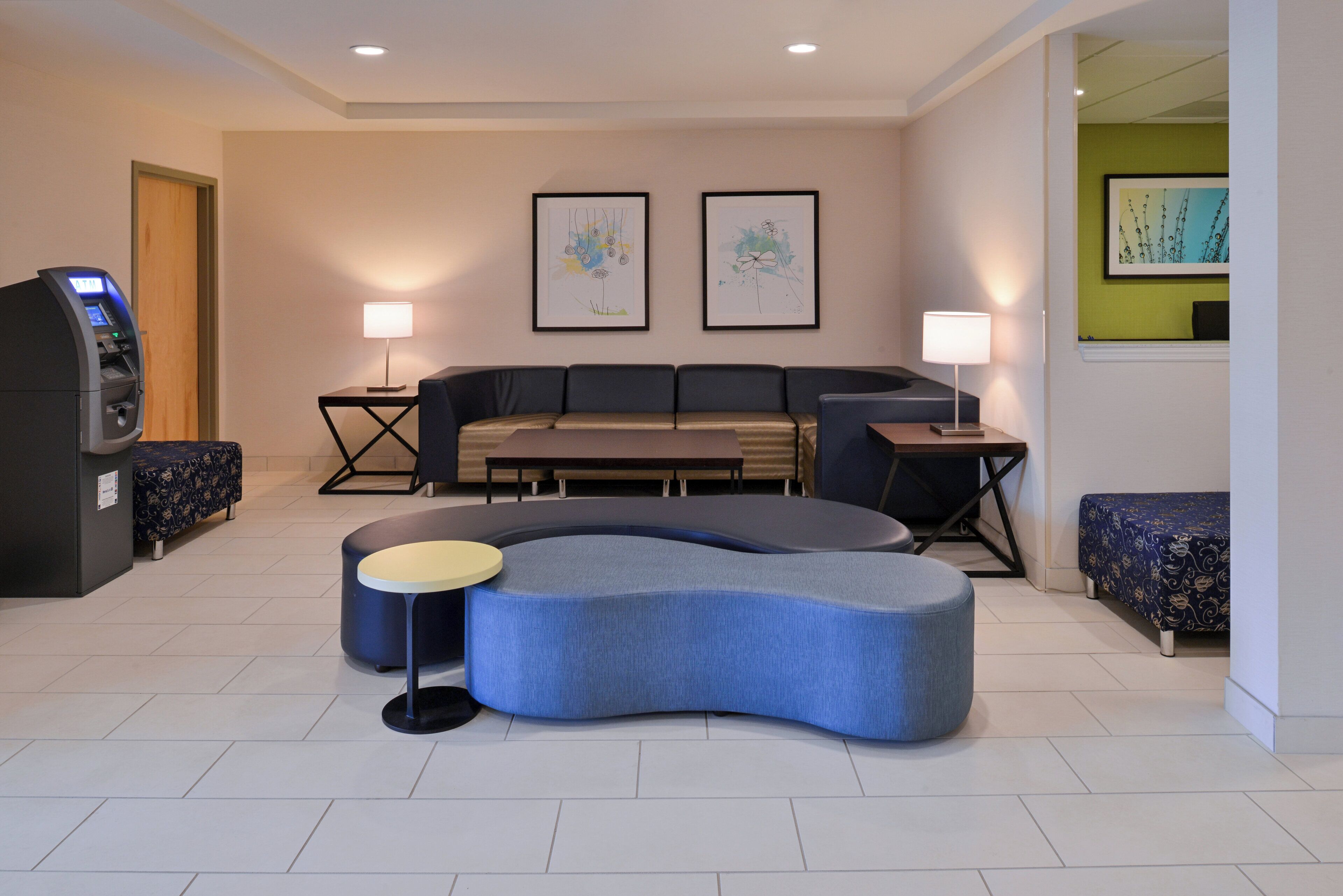 A modern hotel lobby with a sofa, two side tables, a cash machine, and artwork on the walls.
