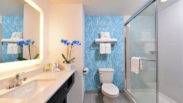 A bathroom with a glass shower enclosure, a white toilet, a sink with a mirror, and a towel rack.