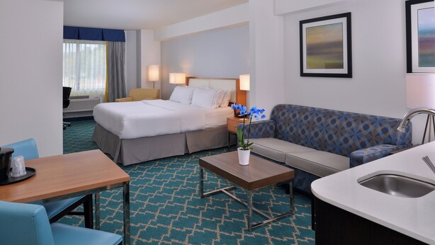 A hotel room with a bed, a sofa, a small table, a sink, and a window with curtains. - Holiday Inn Express & Suites West Ocean City by IHG (Ocean City)
