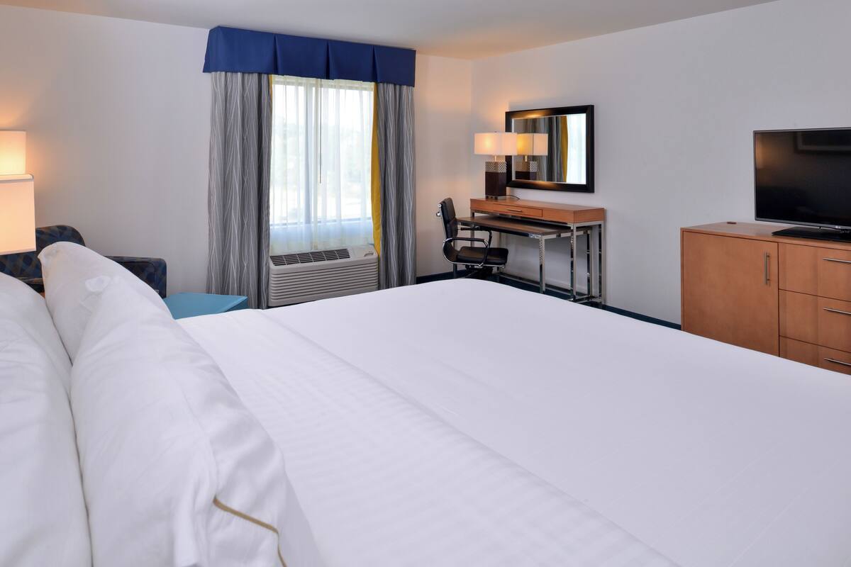 A hotel room with a large bed, a desk with a chair, a television, and a window with curtains.