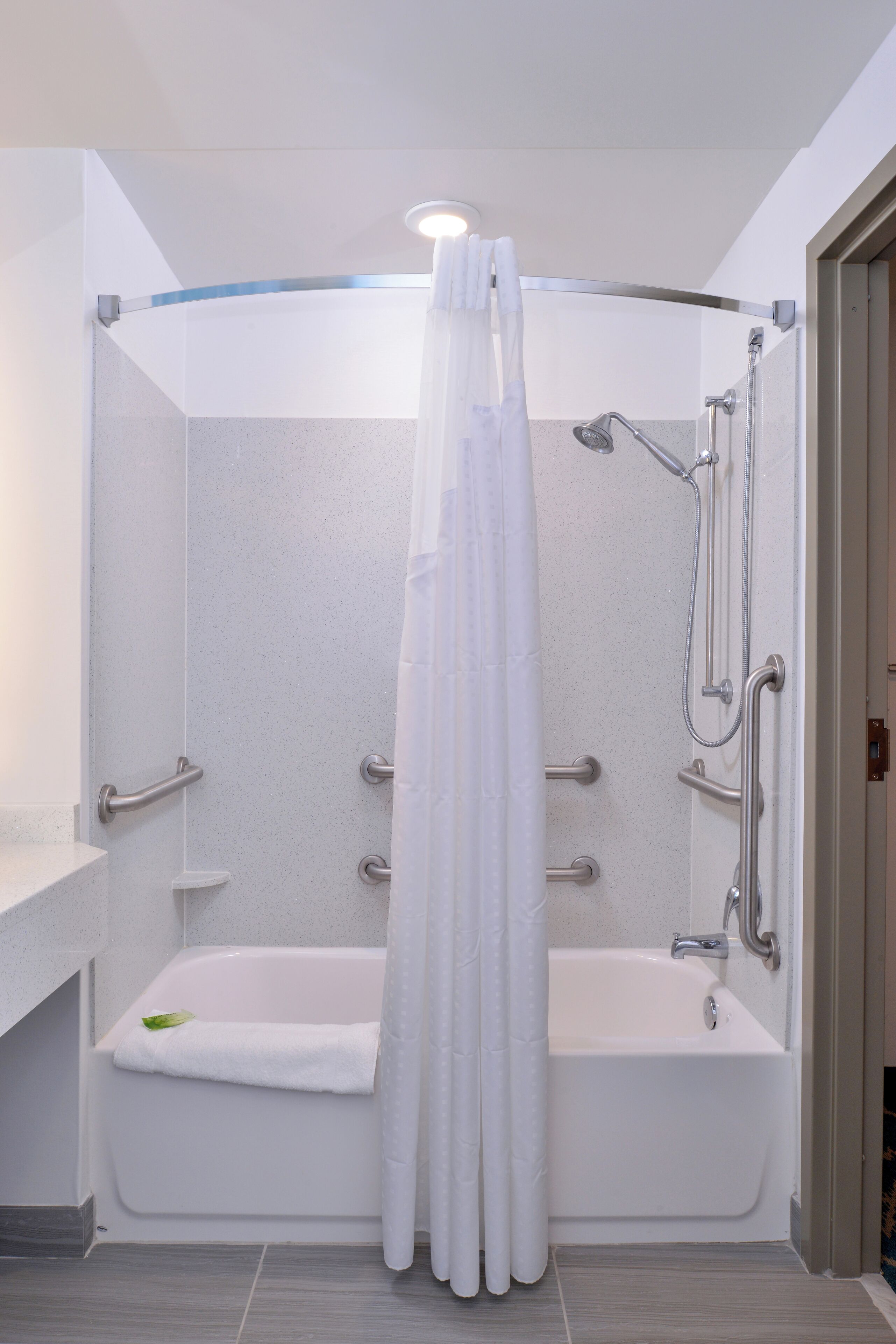Una ducha a ras de suelo con bañera, cabezal de ducha y barra de apoyo.